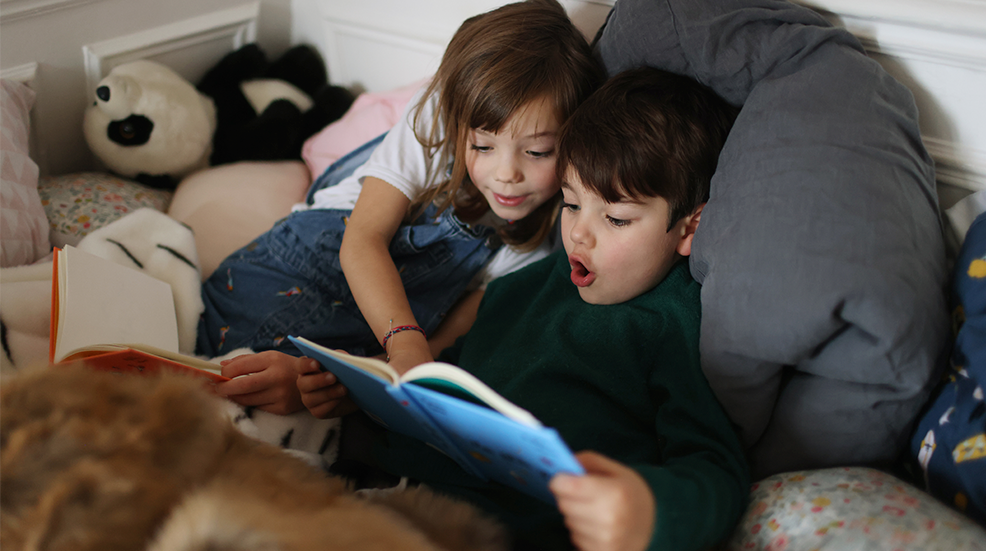 A brother and a sister reading books in the bedroom